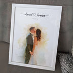 Watercolor-style portrait of a couple kissing, in a white frame leaning on a sofa, with their names and a date above