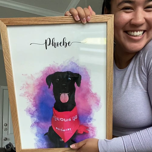 A smiling woman holding a framed portrait of her dog