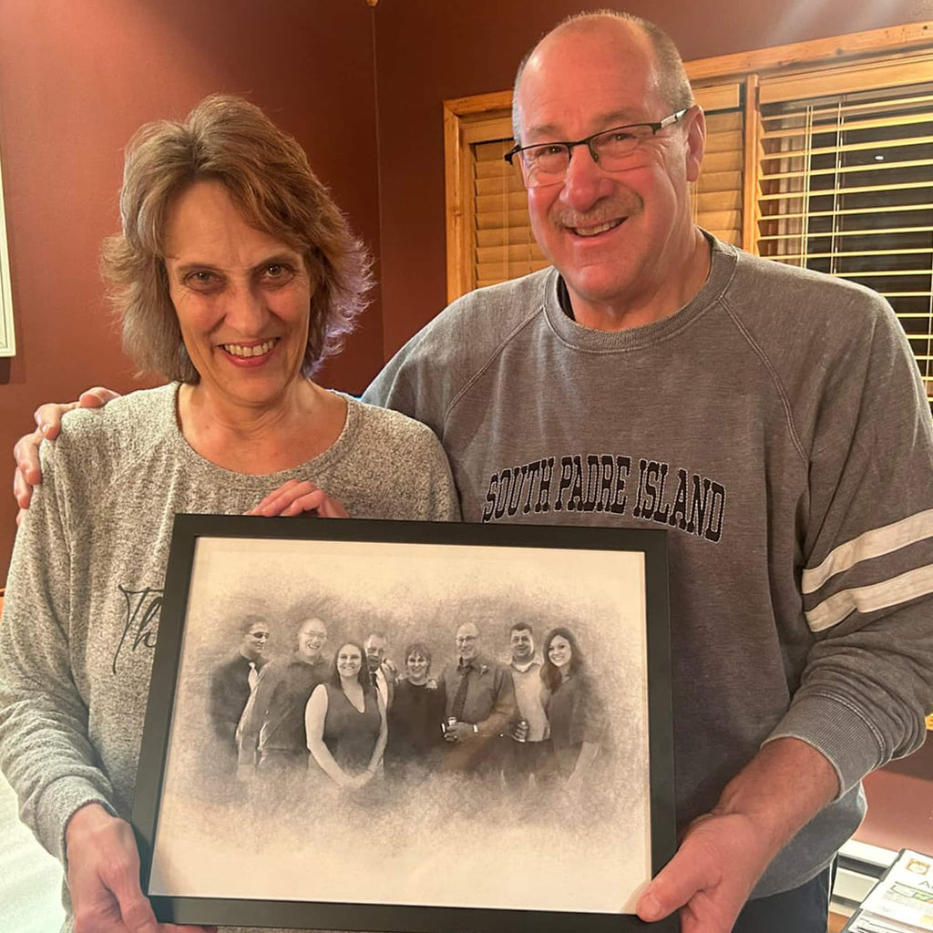 A smiling older couple hold a black-framed sketch-style portrait of a large group of people