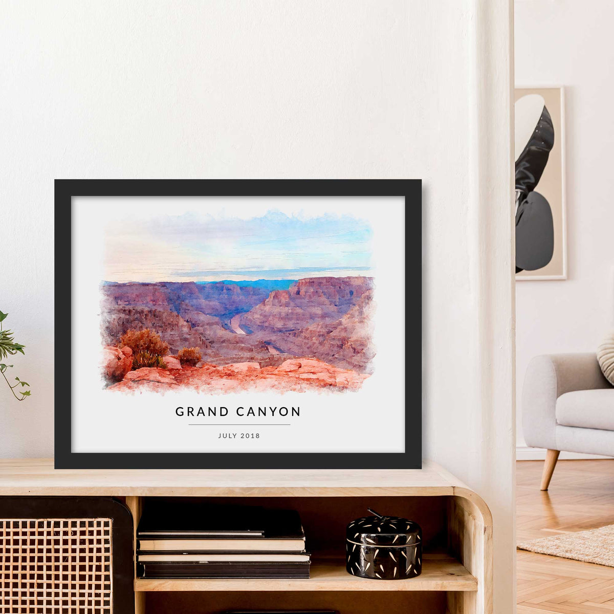 Watercolor-style portrait of the Grand Canyon, framed in black and leaning on a wooden sideboard