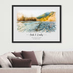Watercolor-style portrait of a stony riverbank with sunlit trees and hills, framed in black above a sofa, names beneath